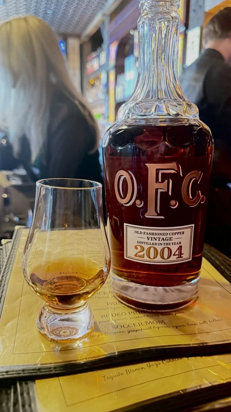 A pour of O.F.C. Vintage 2004 bourbon in a Glencairn glass next to the bottle.