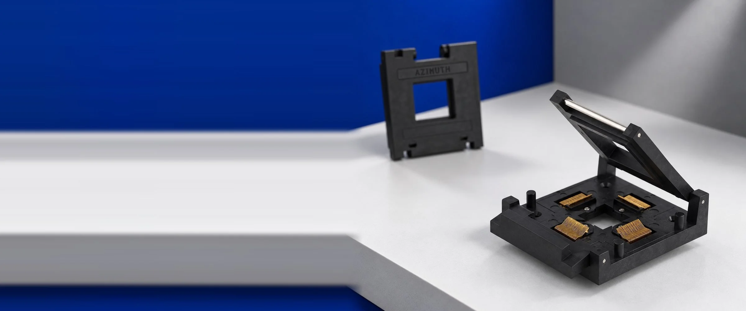 Azimuth Electronics open-lid IC test socket with gold contacts, with an Azimuth branded lid frame in the background