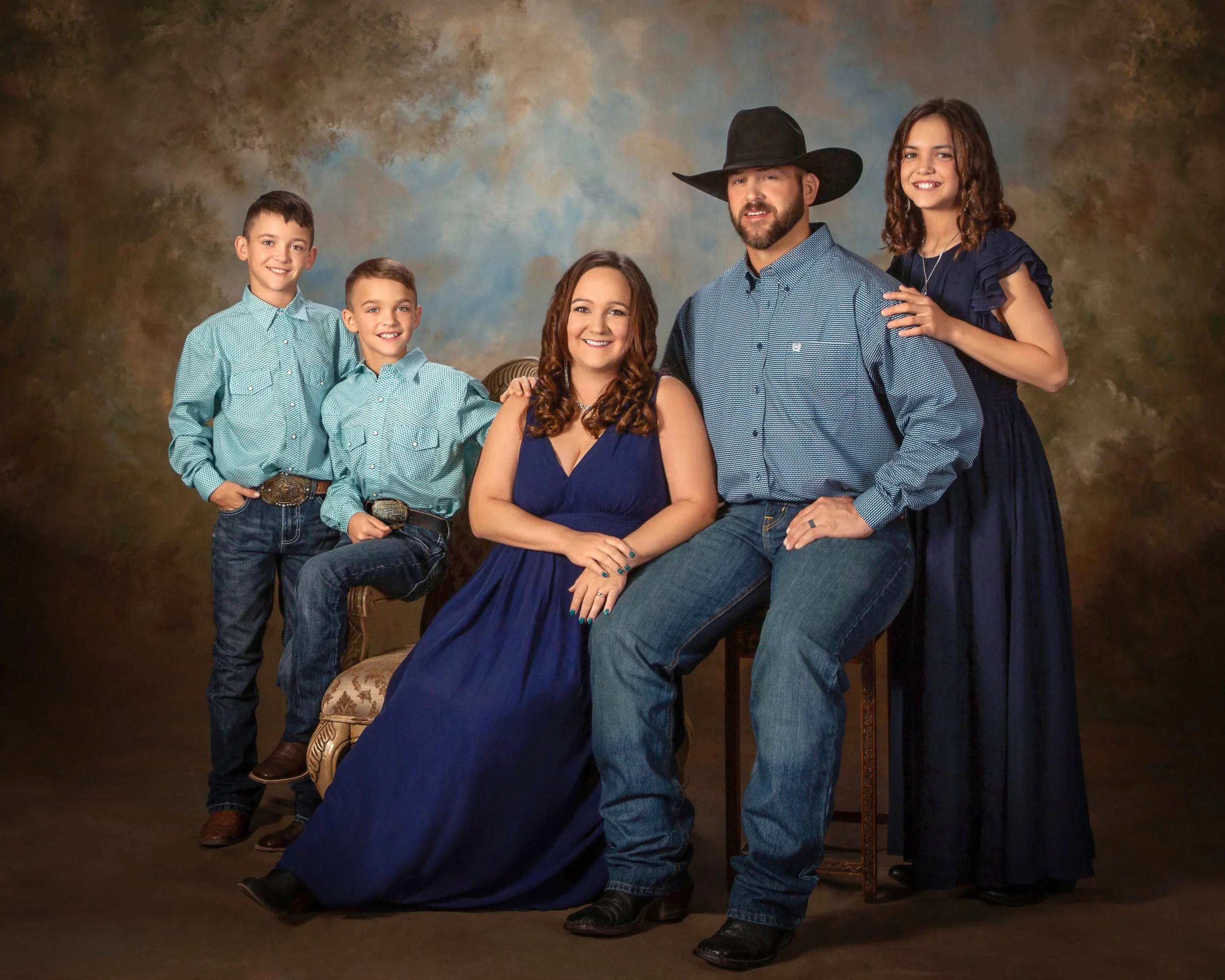 A family of five in western attire, the father in a cowboy hat, gathered around a seated mother in a navy gown