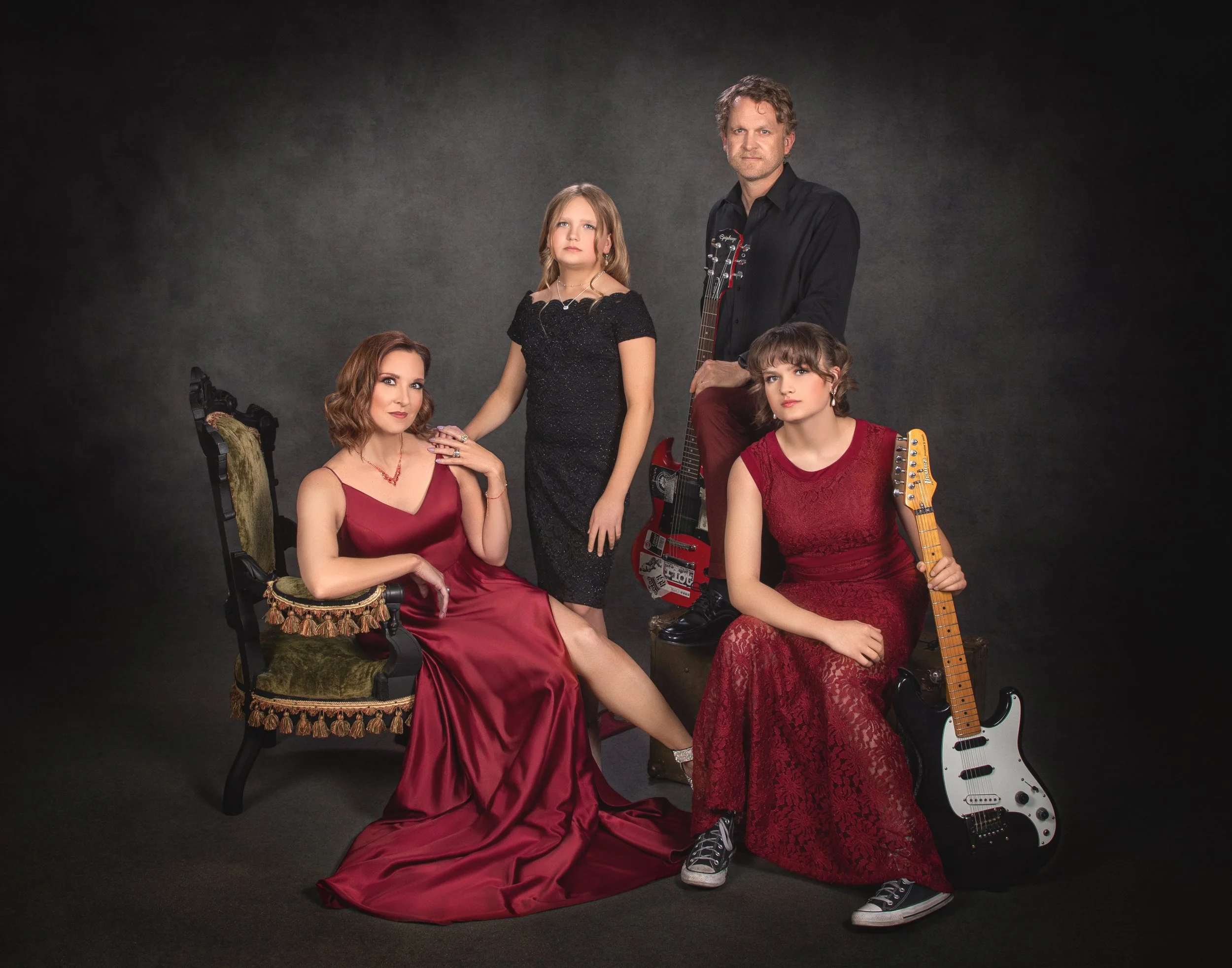 A family of four gathered on an antique settee, one holding an electric guitar
