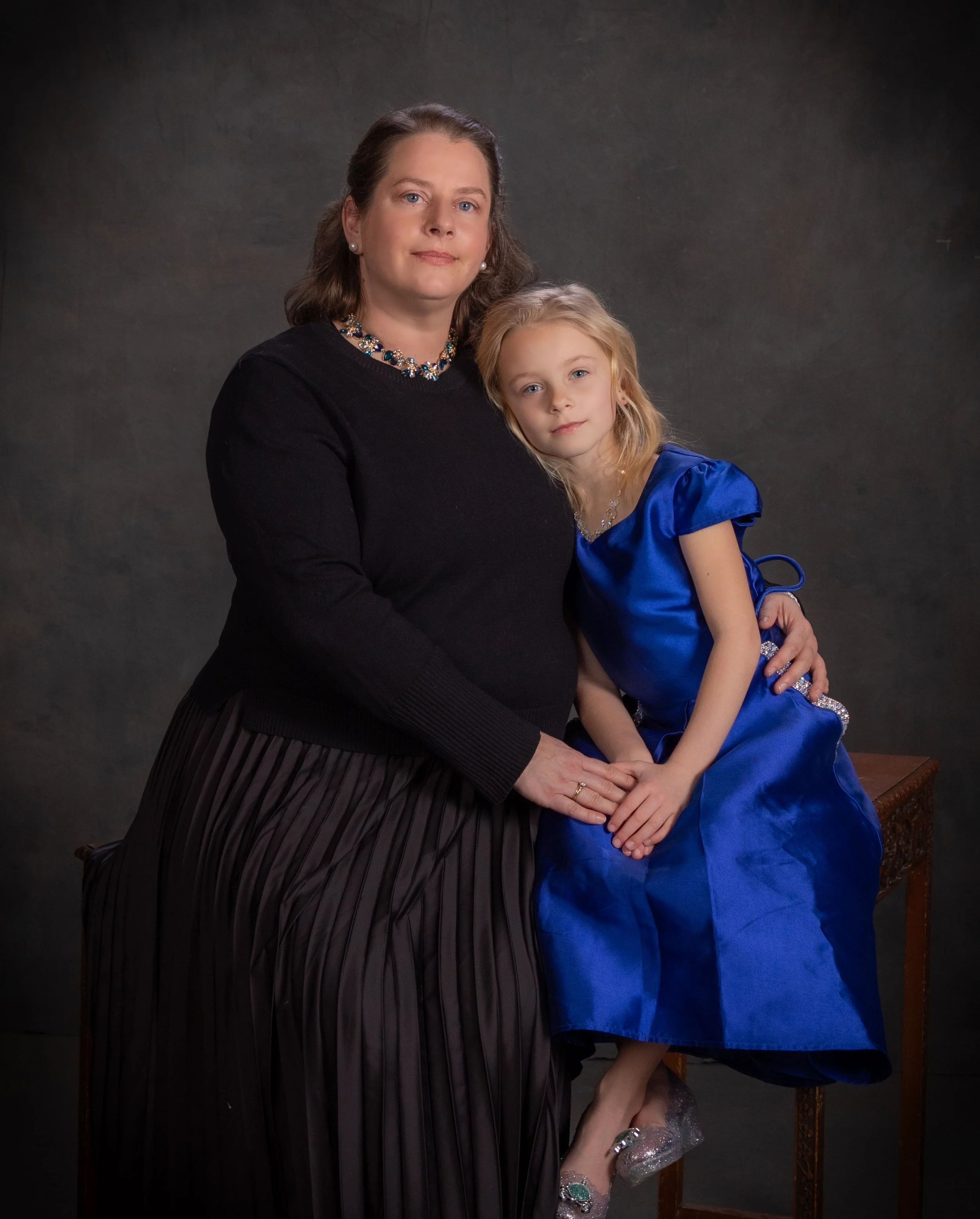 Fine art portrait of a mother in black embracing her young daughter in a royal blue dress