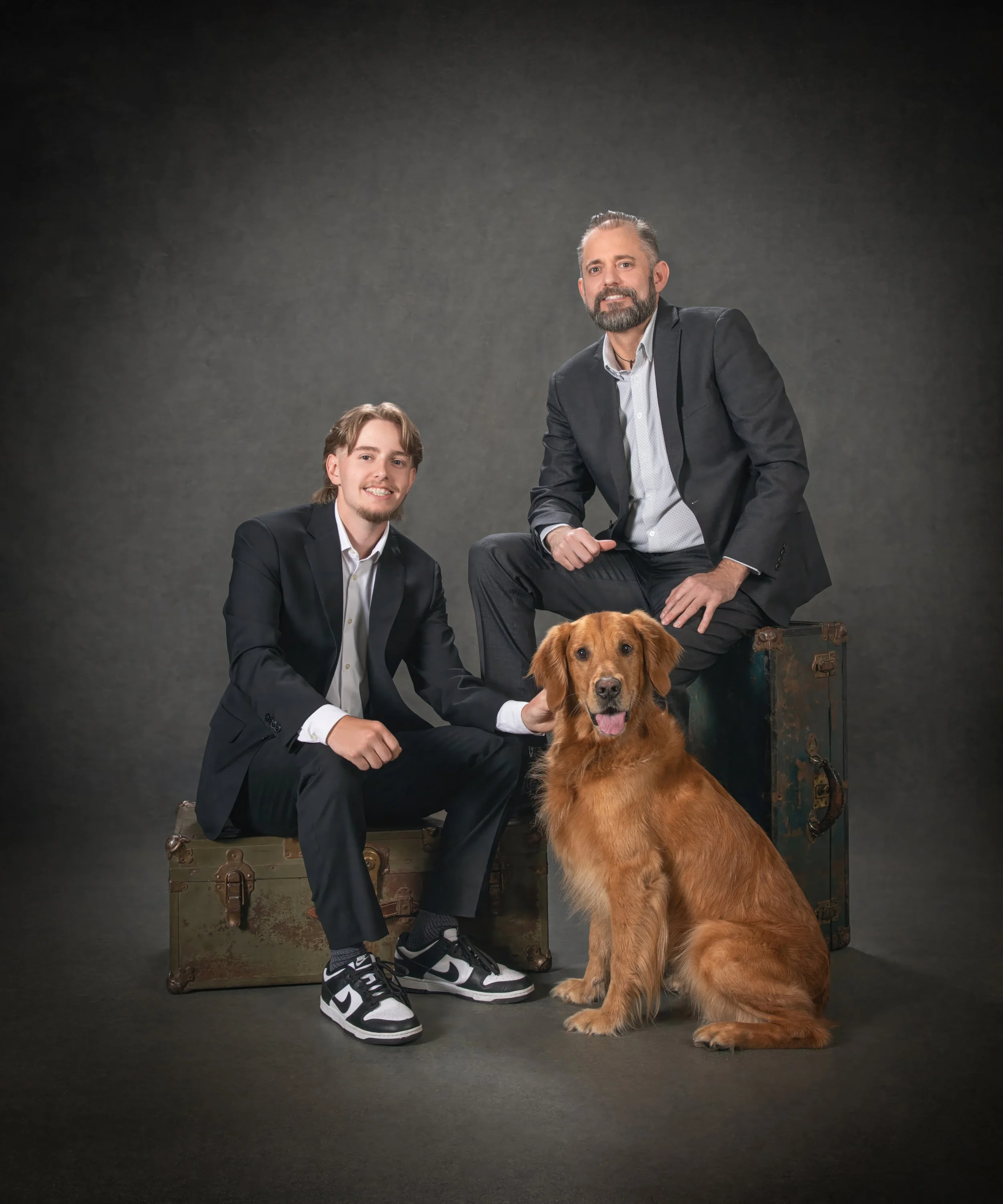 A father and son seated together with their golden retriever