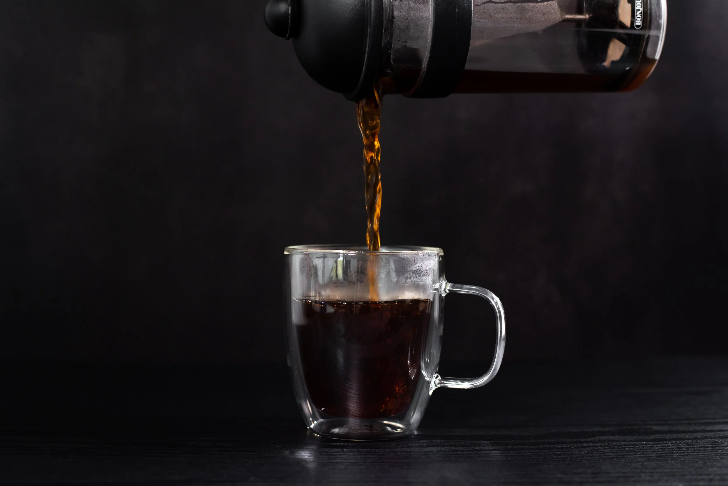 Pure Grind coffee pouring from a French press into a glass cup