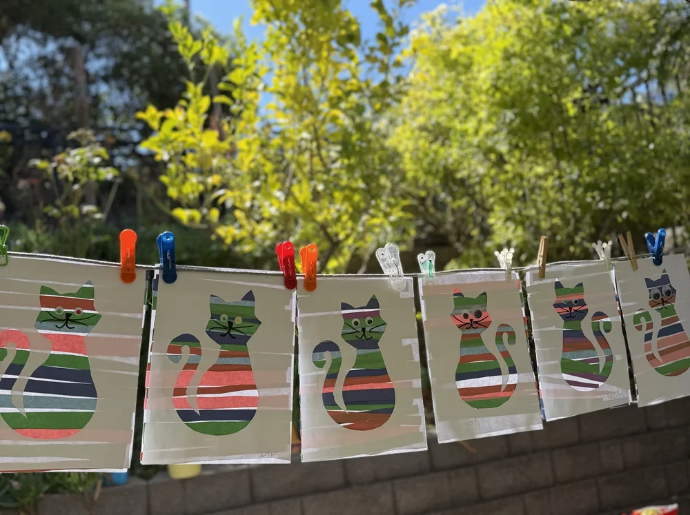 Colorful artwork hanging on a line in the sunny Mila-Ma garden