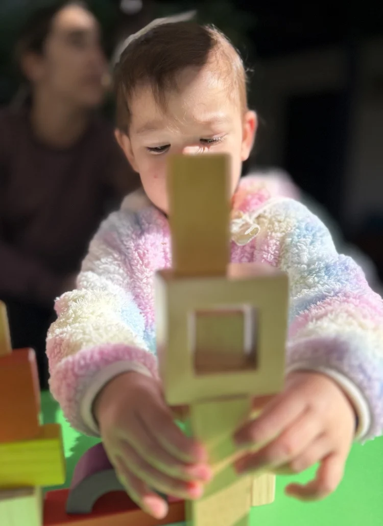 A child building a tower with wooden window blocks
