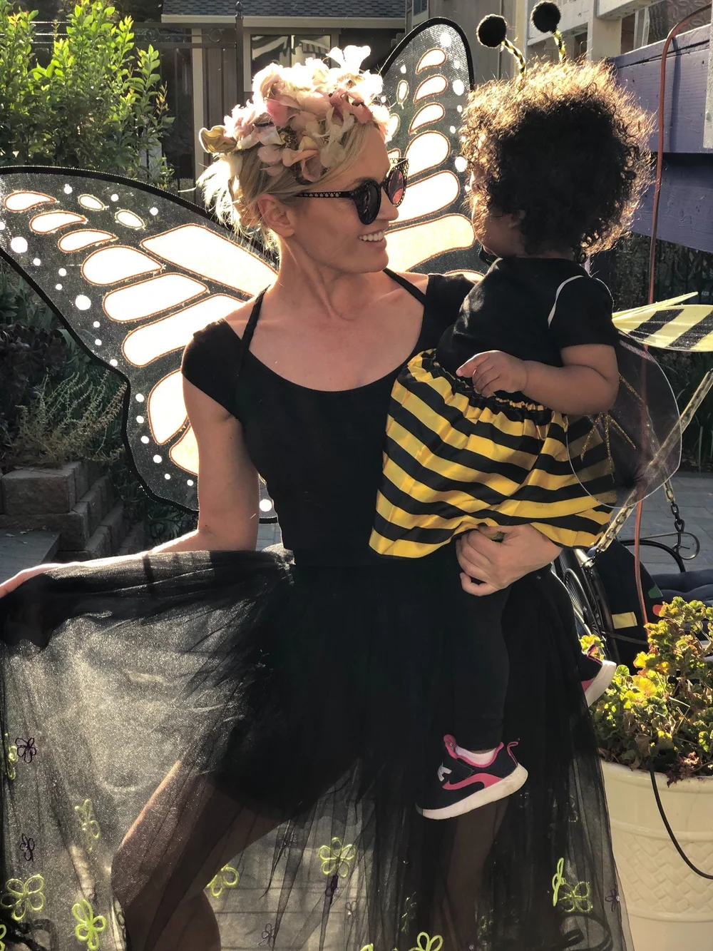 An adult in butterfly wings holding a child dressed as a bee in the garden