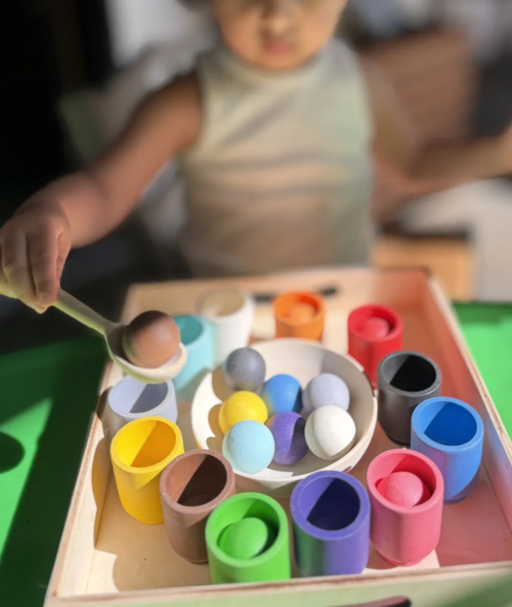 A child sorting wooden rainbow balls and cups