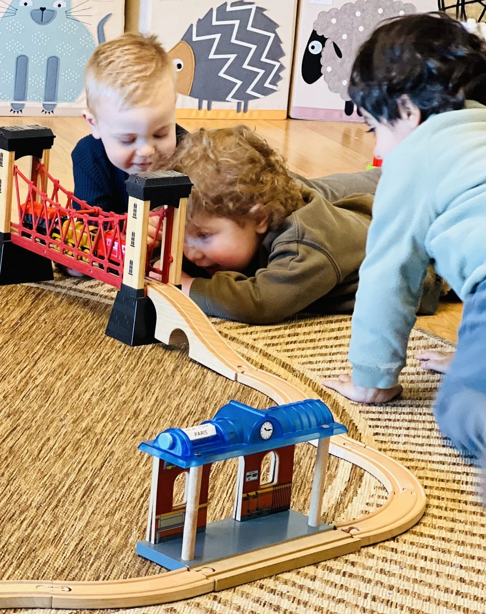 Three children playing together with a wooden train track in the playroom