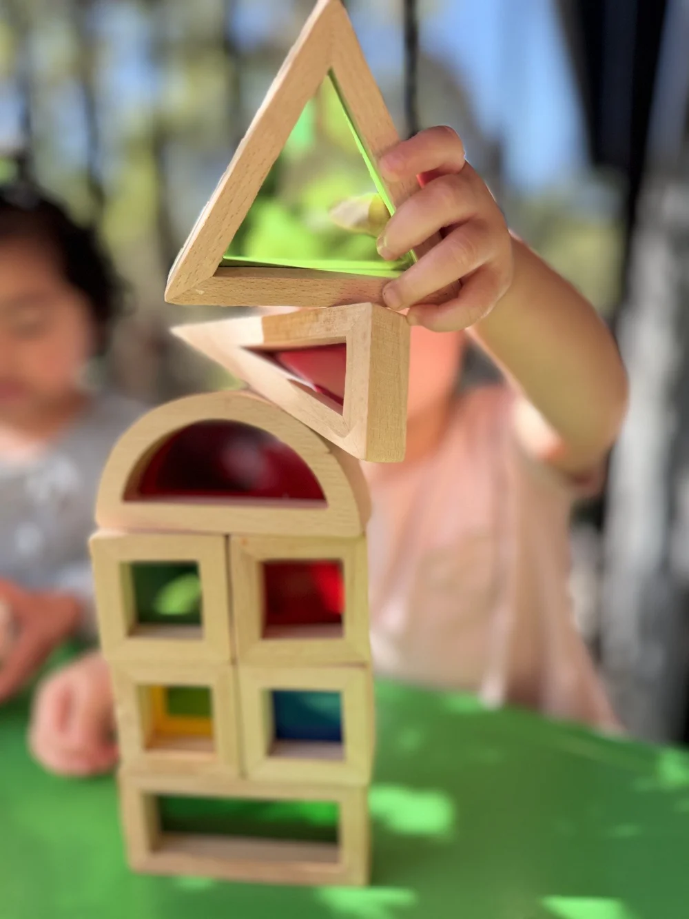 Little hands balancing translucent wooden shapes into a tower