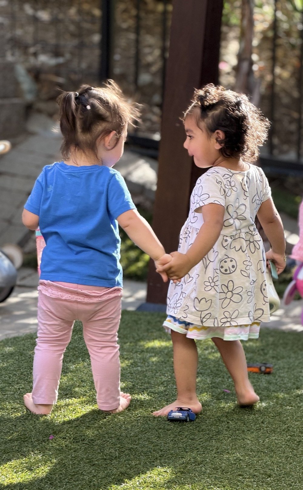 Two children holding hands in Mila-Ma’s outdoor play area