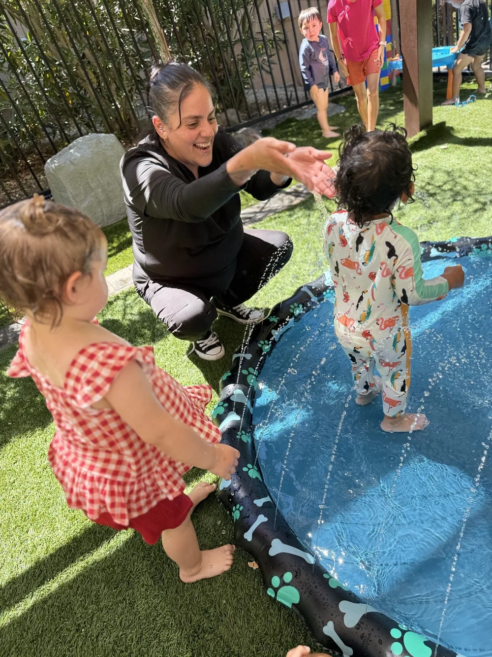 A caregiver and children enjoying a blue outdoor water play mat