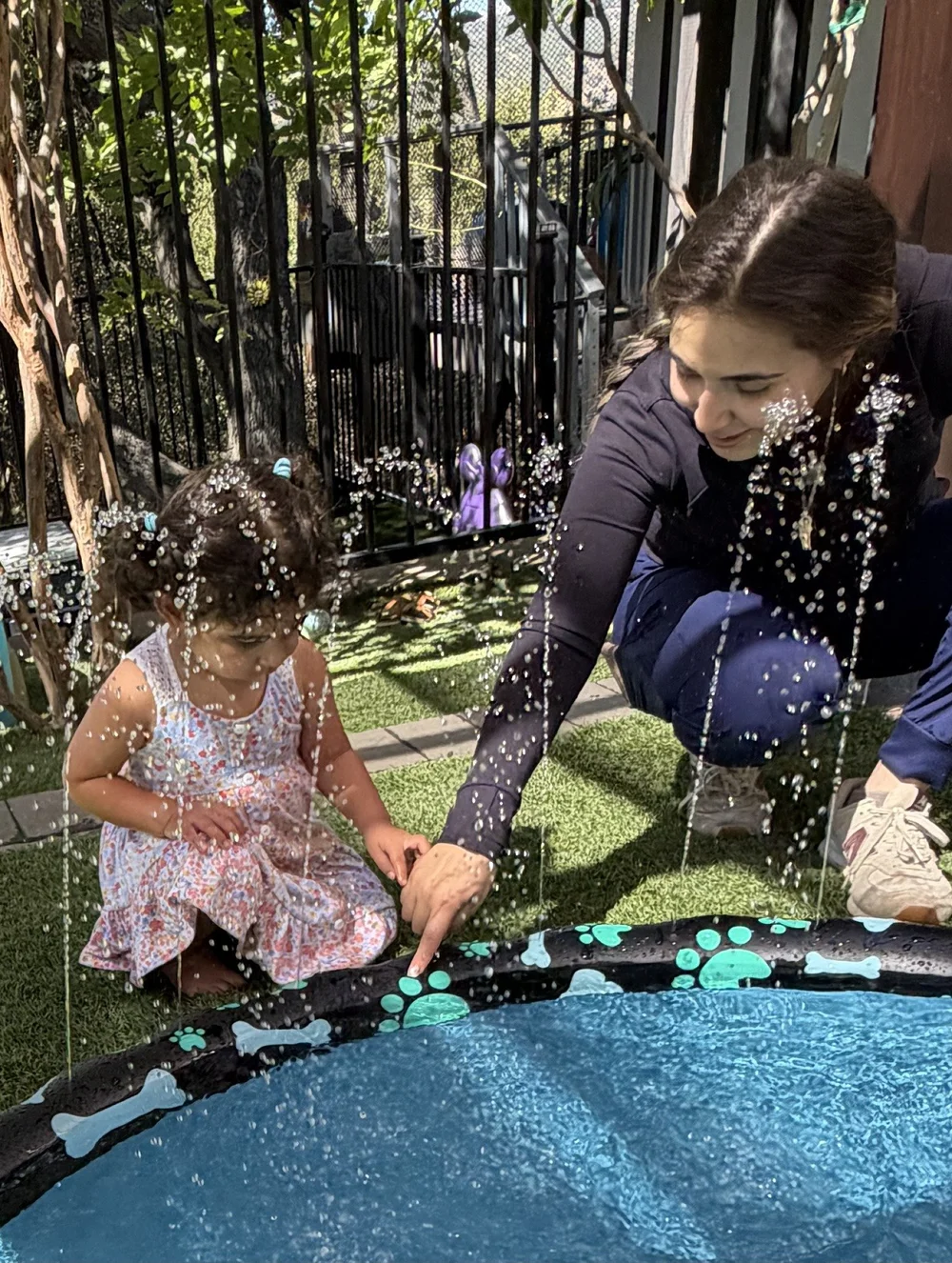 A caregiver staying close as a child explores outdoor water play