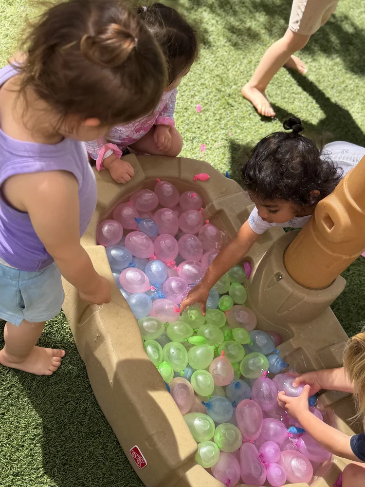 Children exploring colorful water balloons at an outdoor play table