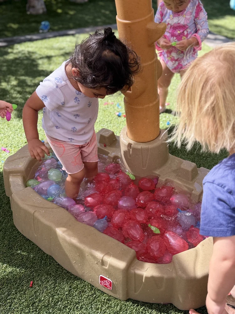 Toddlers investigating water balloons in an outdoor tray