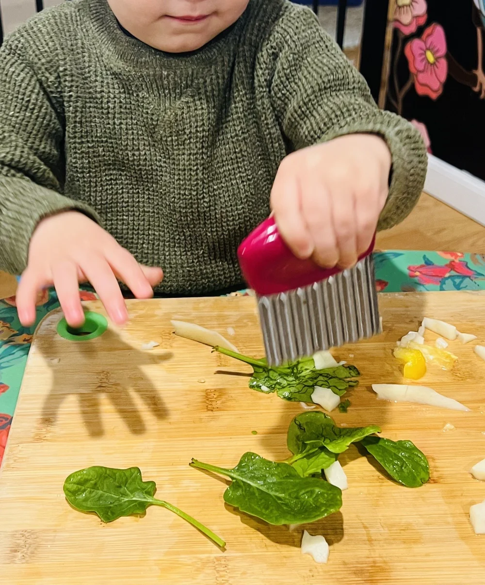 A child using a crinkle cutter to prepare ingredients on a wooden board