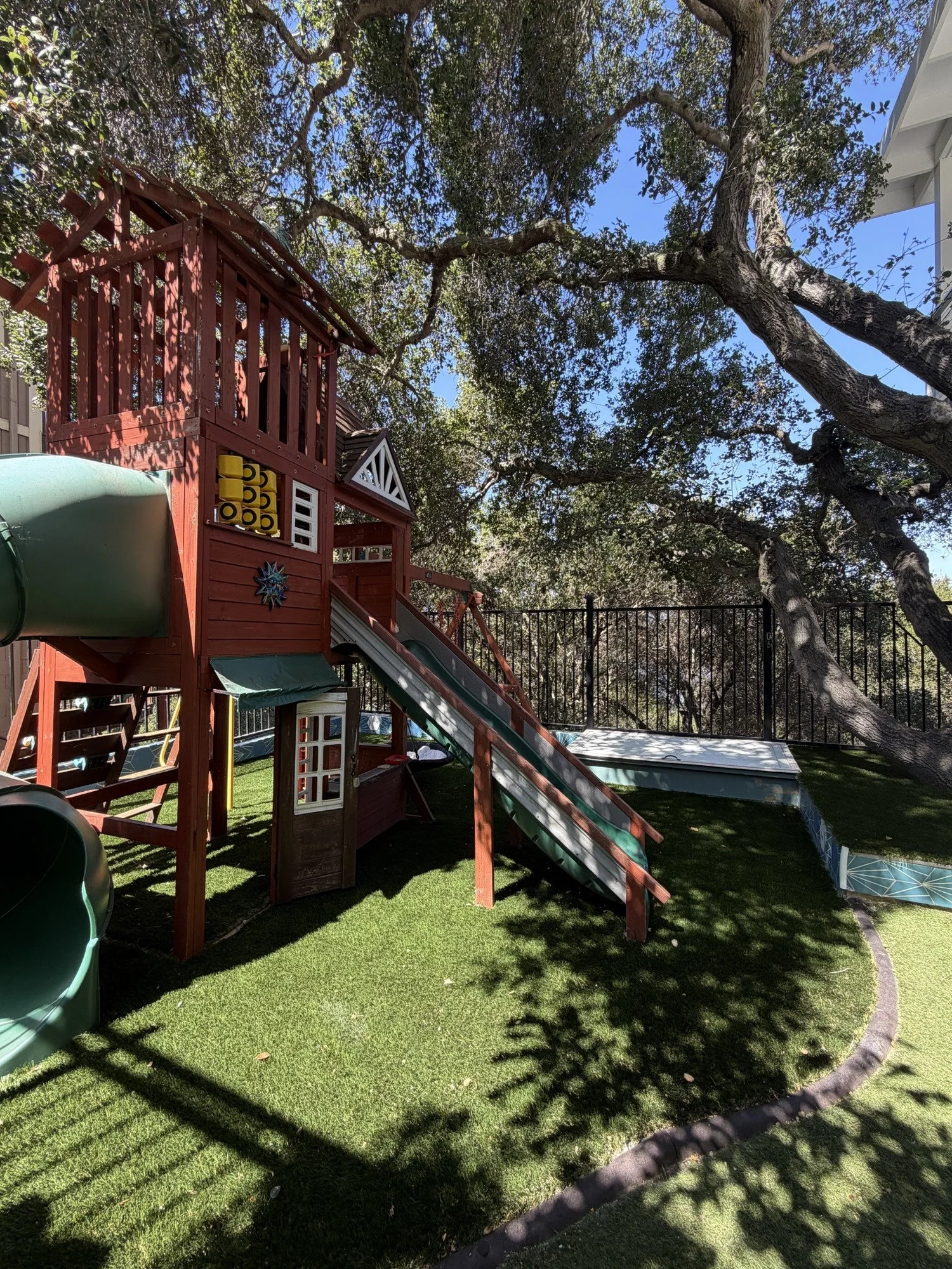 A closer view of the wooden playground structure and slides beneath tree branches