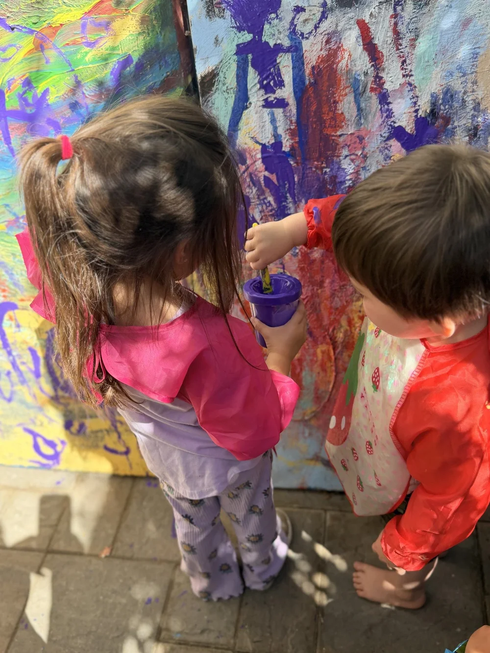 Two children painting together on a large outdoor canvas