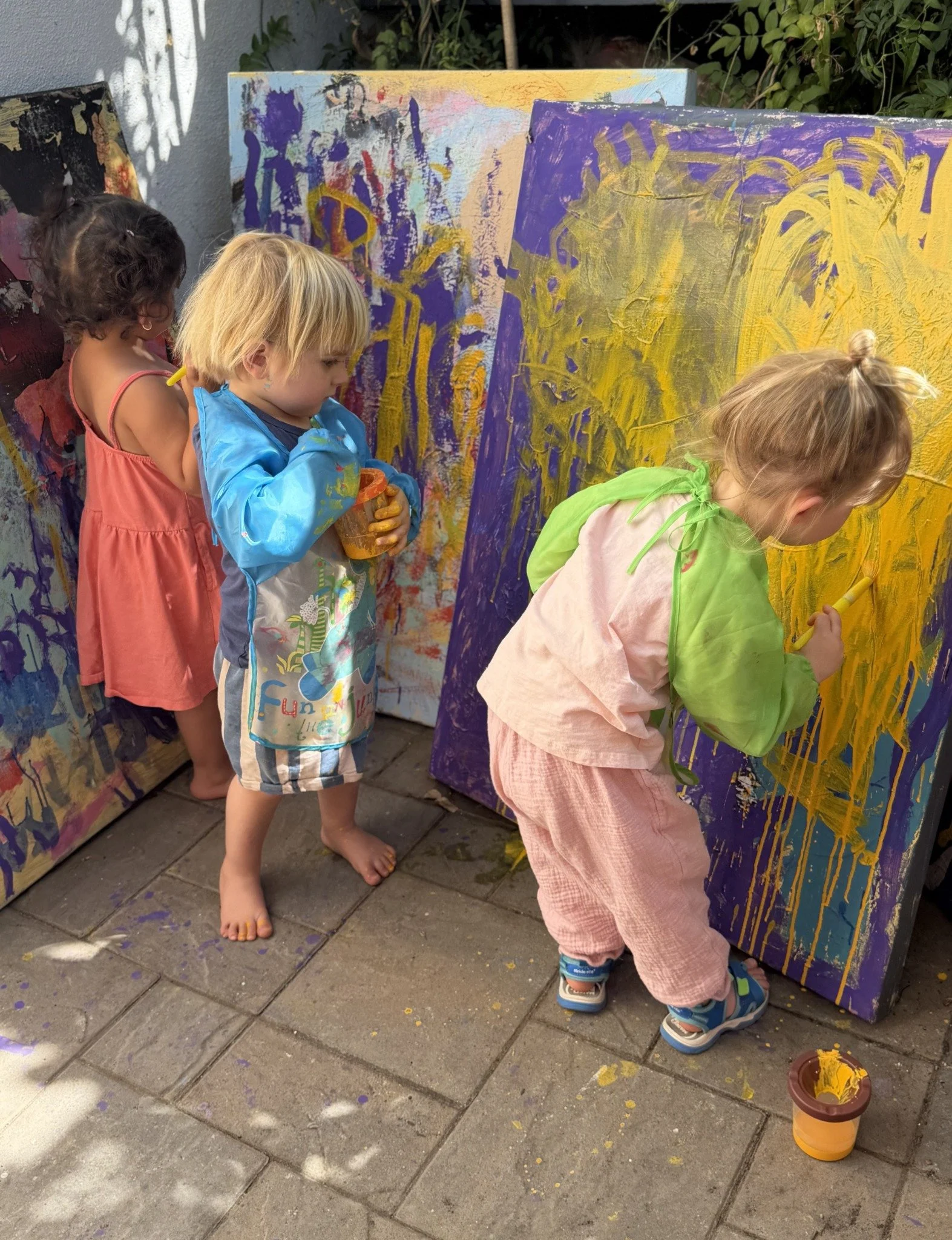 Children painting a large outdoor canvas with bright yellow and purple paint