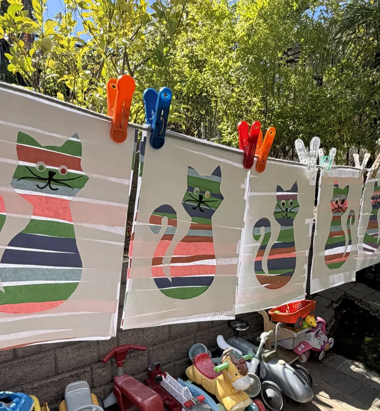 A colorful striped paper cat collage hanging from clips