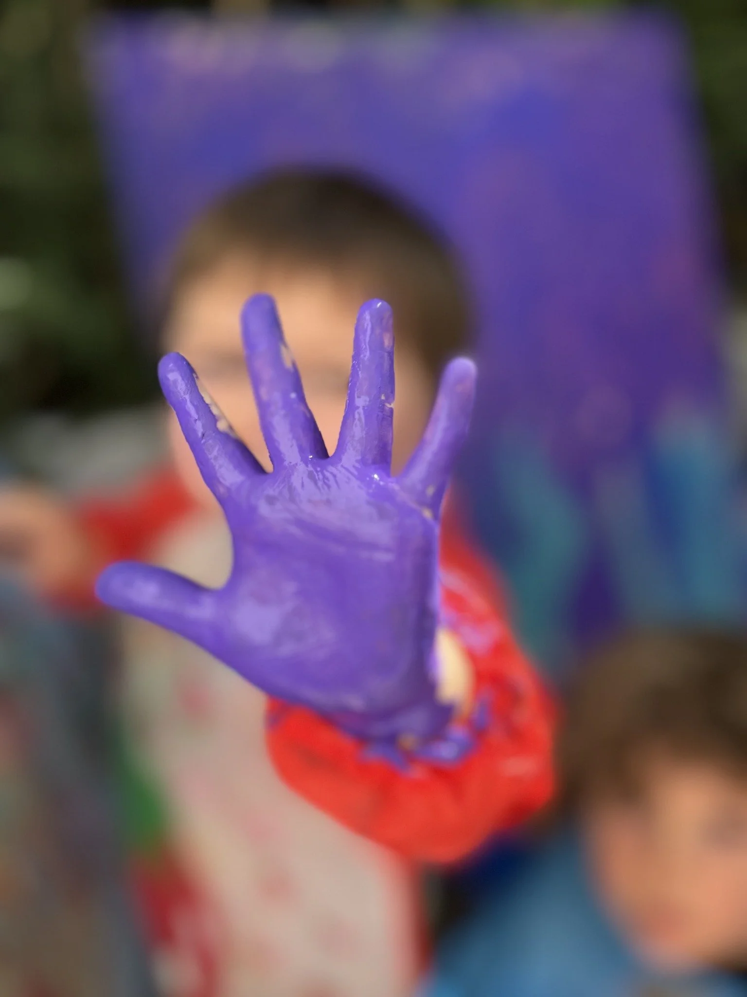 A child holding up a hand covered in purple paint