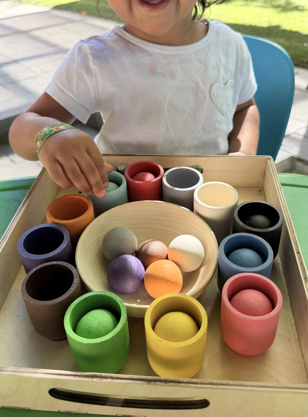 A child exploring rainbow wooden balls and matching cups