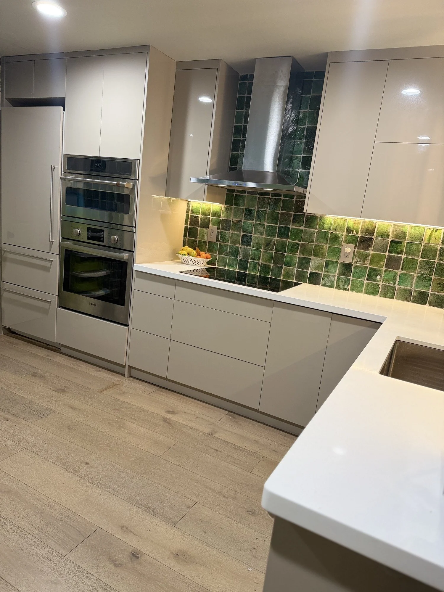 Baba’s kitchen with green tile, warm lighting and pale cabinetry