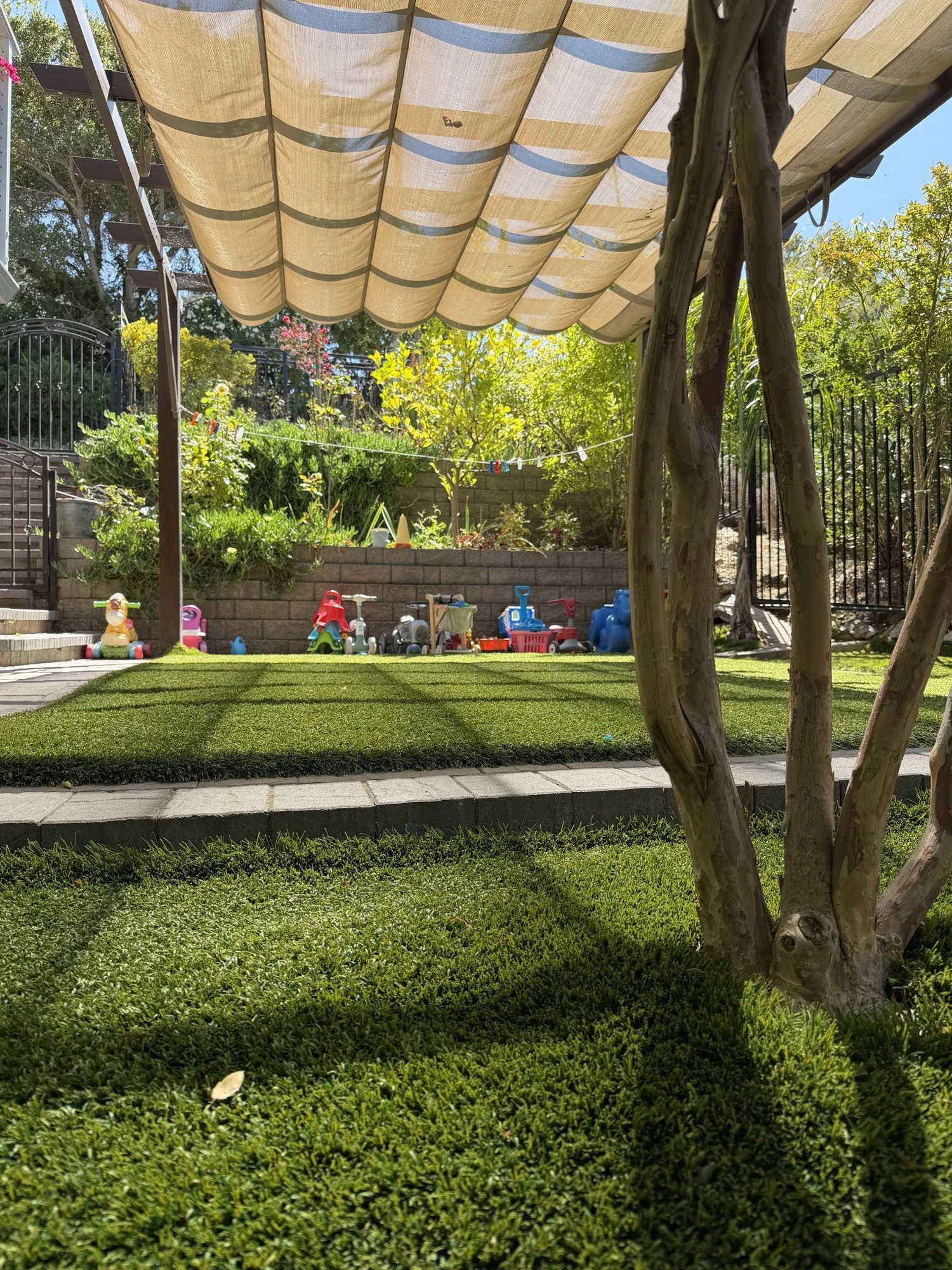 The Mila-Ma courtyard with a fabric canopy, green play space, and a row of ride-on toys