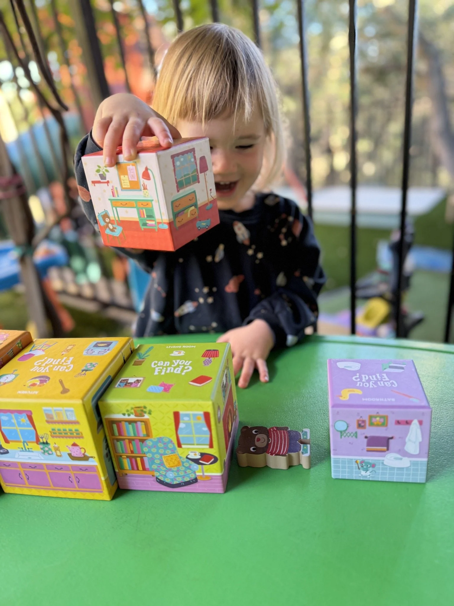 A smiling child stacking colorful illustrated cubes outdoors