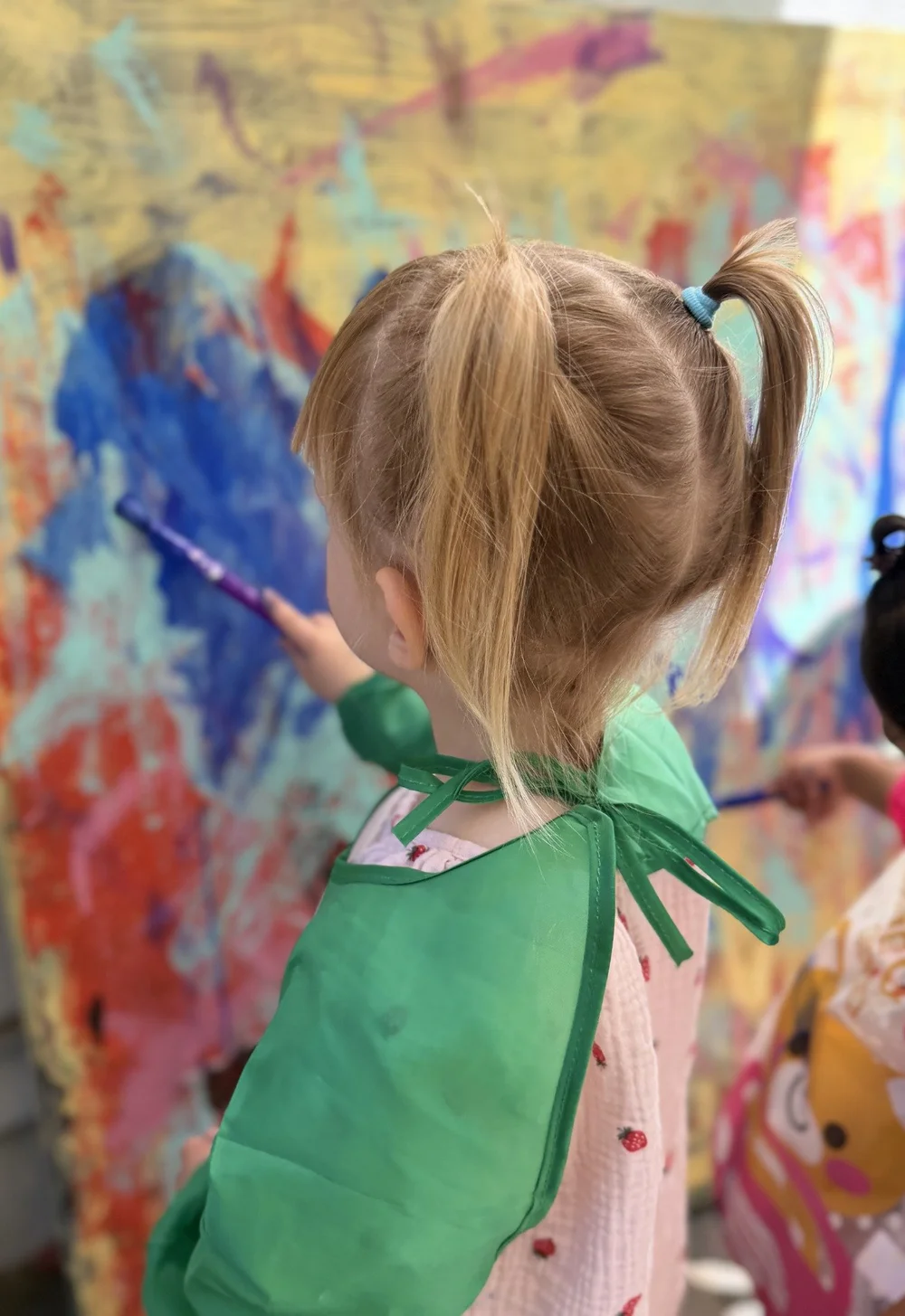 A child in a green smock concentrating on a colorful painting