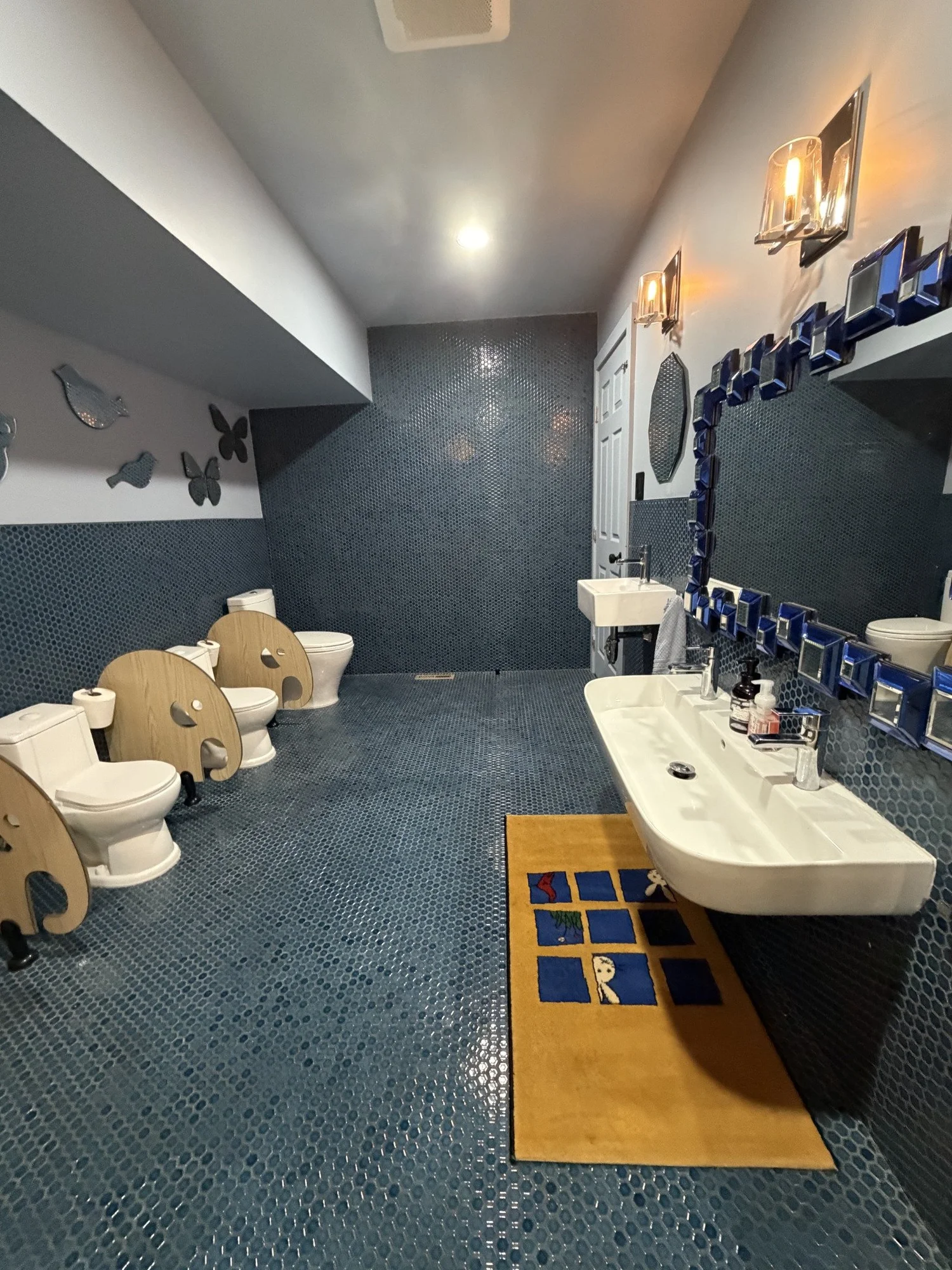 Mila-Ma children’s bathroom with blue mosaic tiles, small toilets and a low handwashing sink