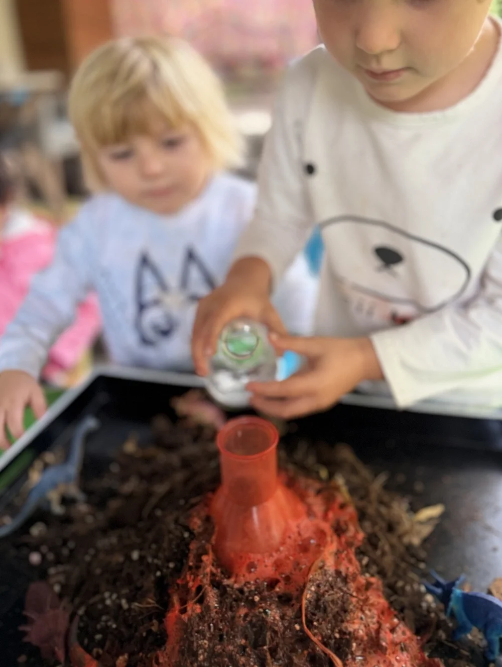 A child pouring into a model volcano in a soil-filled tray