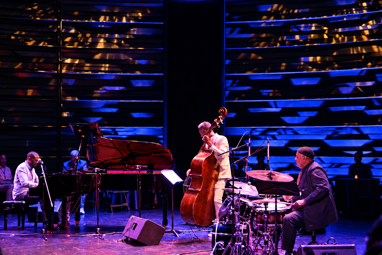 Udobi trio performing with grand piano, upright bass and drums under blue and purple stage lights