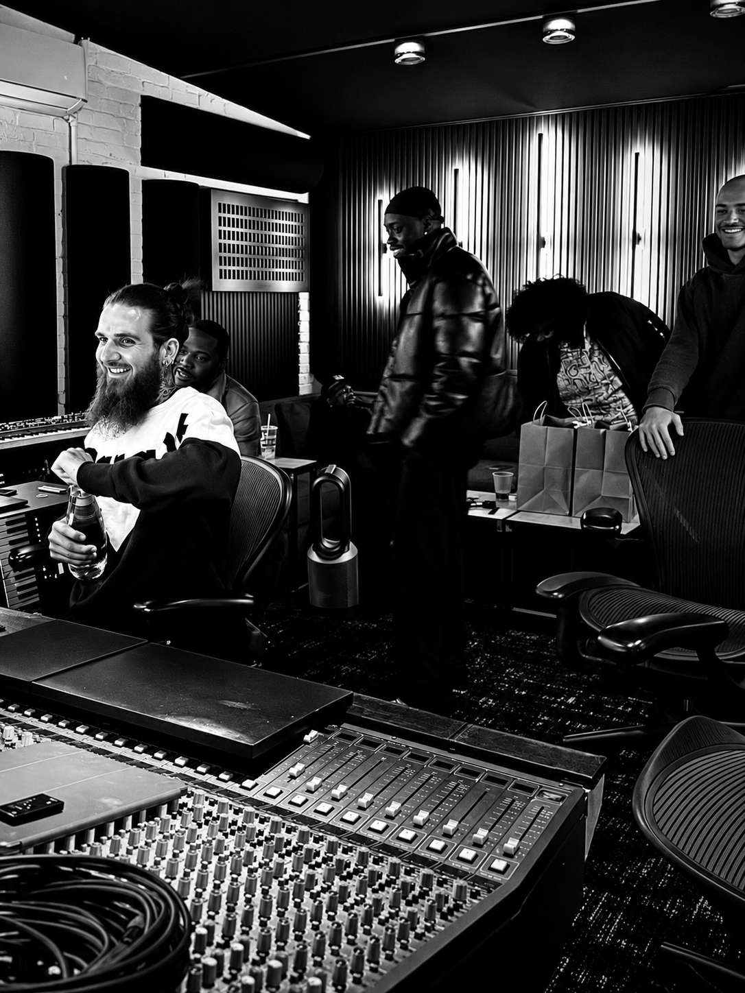 Black and white candid of Udobi and musicians gathered in a recording studio beside a mixing console