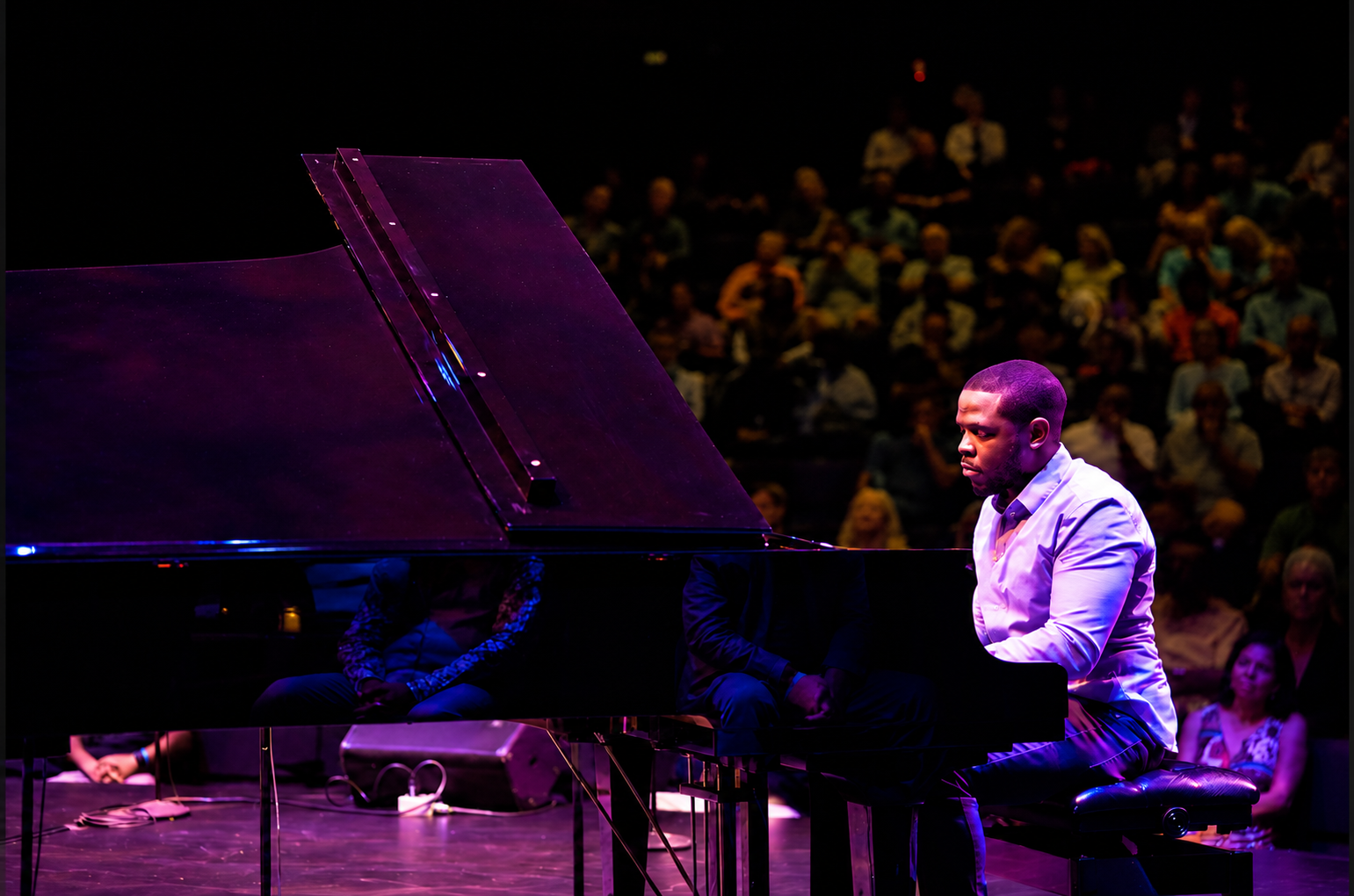 Udobi performing at a grand piano under purple stage lighting before an audience
