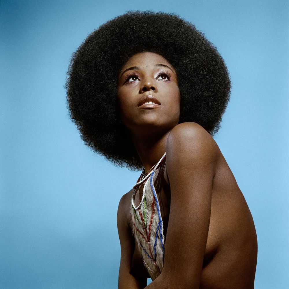 A model photographed against a bright blue background, hair worn natural