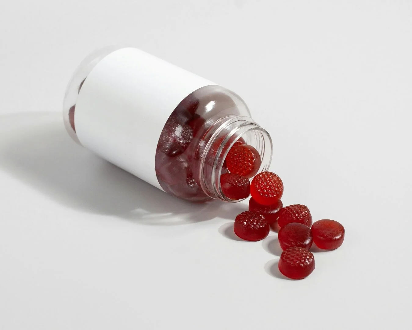 An open bottle spilling red gummies onto a light background.