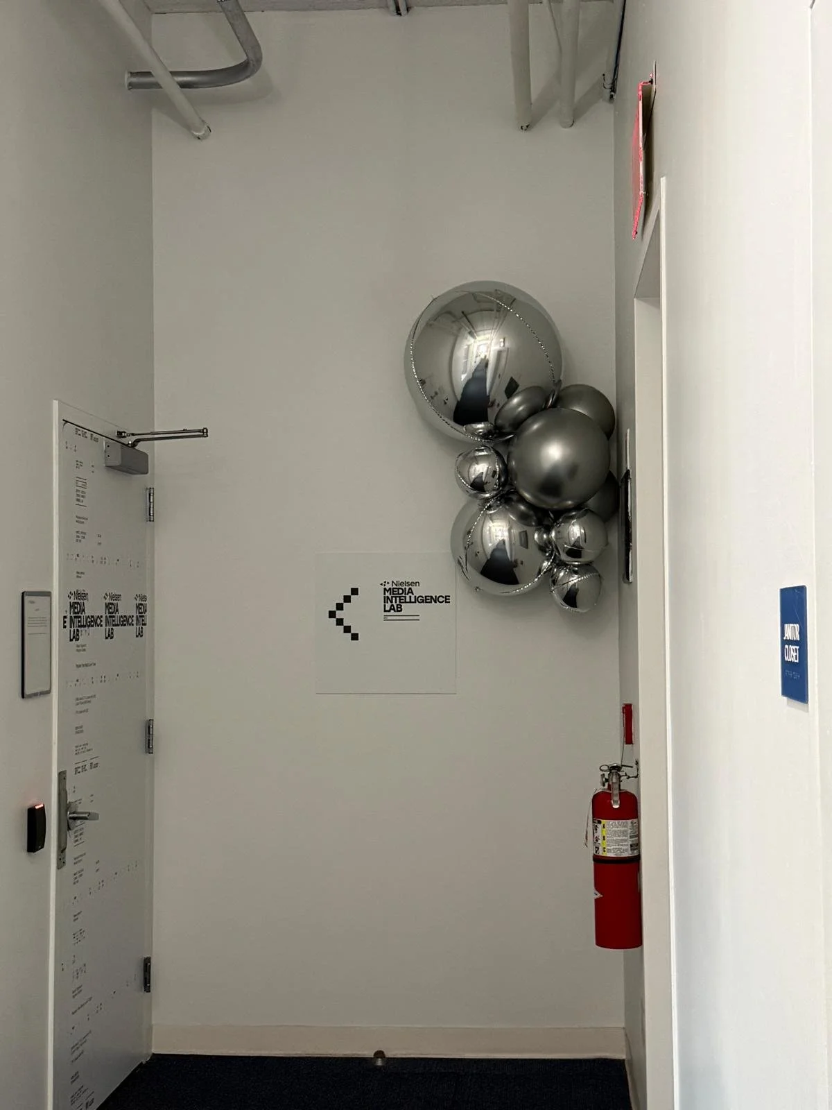 Silver balloon cluster beside the Nielsen Media Intelligence Lab sign in a Chelsea NYC hallway