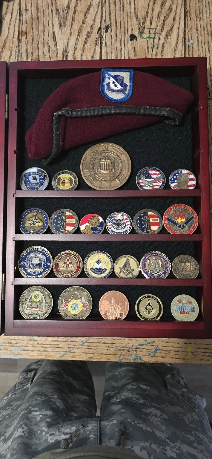 My maroon beret and challenge coins displayed in a wooden case.