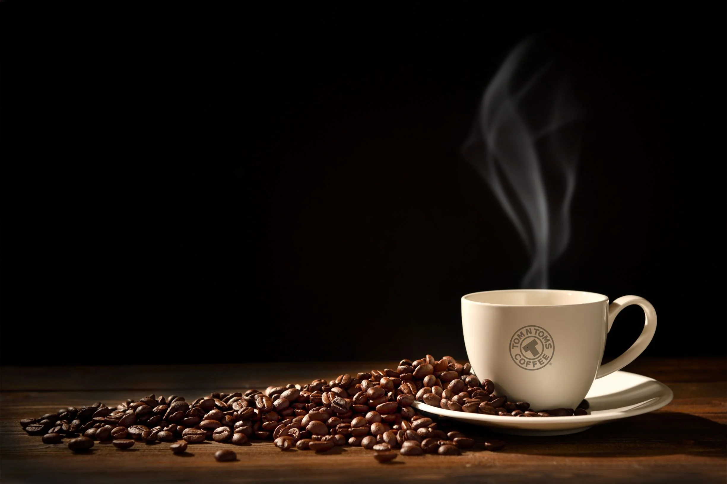 Steaming coffee in a TOM N TOMS cup beside roasted coffee beans