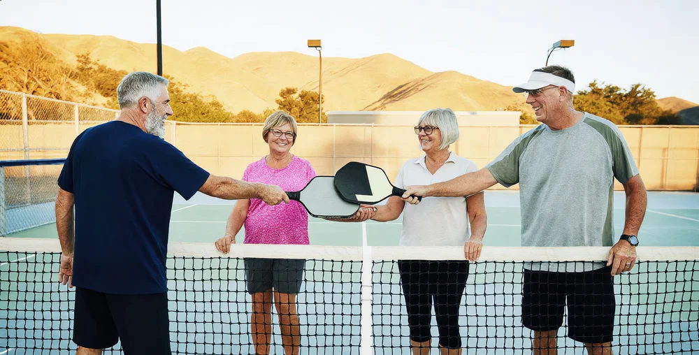 Two doubles teams tapping paddles over the net after a pickleball match