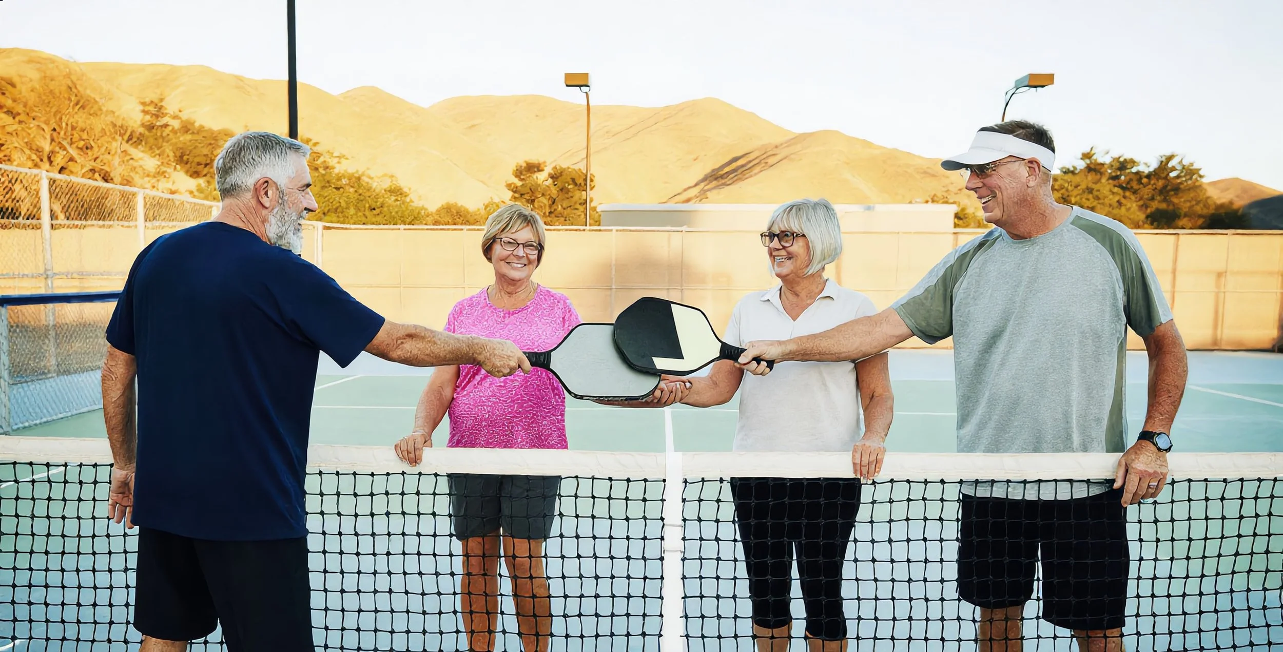 Two doubles teams tapping paddles over the net after a pickleball match