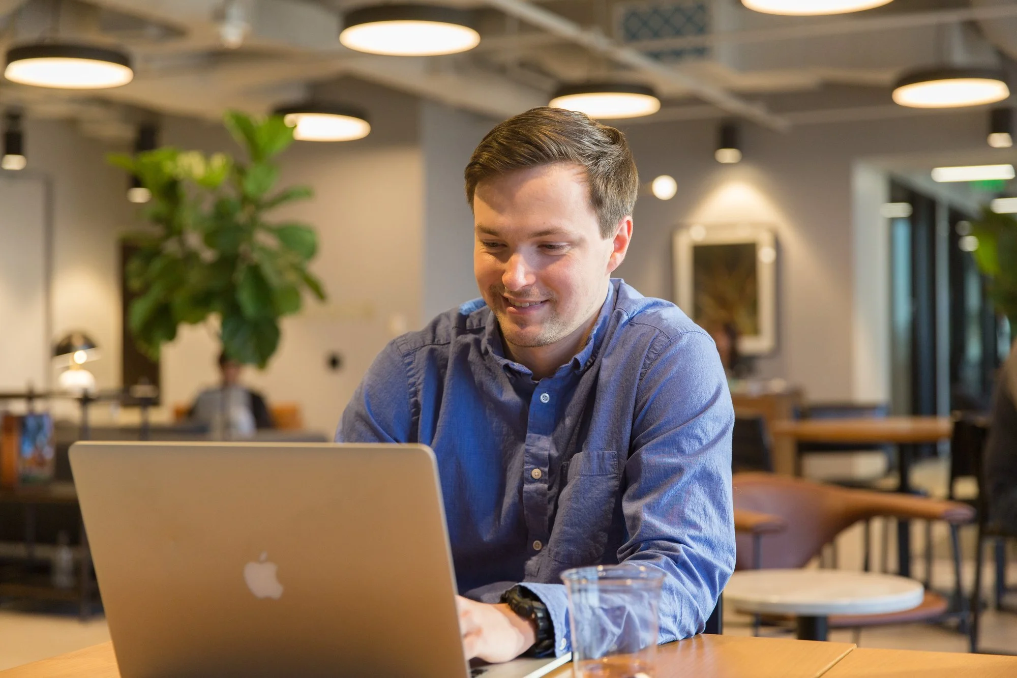 IT professional smiling while signing in to a MacBook at a table in a bright office