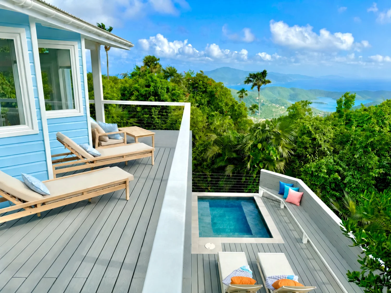 Lounge chairs on Vela Vista’s upper deck, with the railed plunge pool deck below and green hills sloping down to the bay