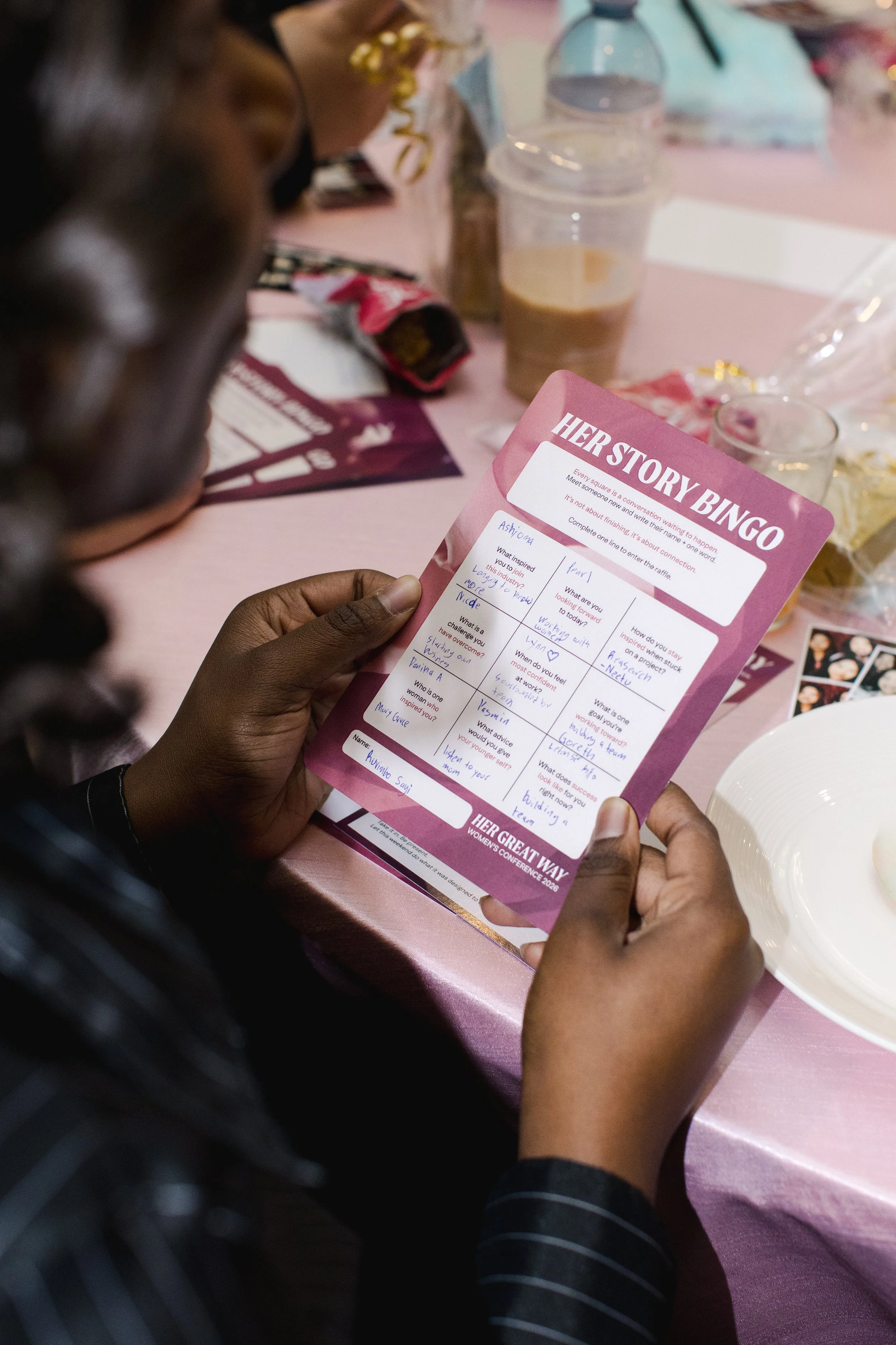 An attendee holding a Her Story Bingo card with handwritten names and one-word answers.
