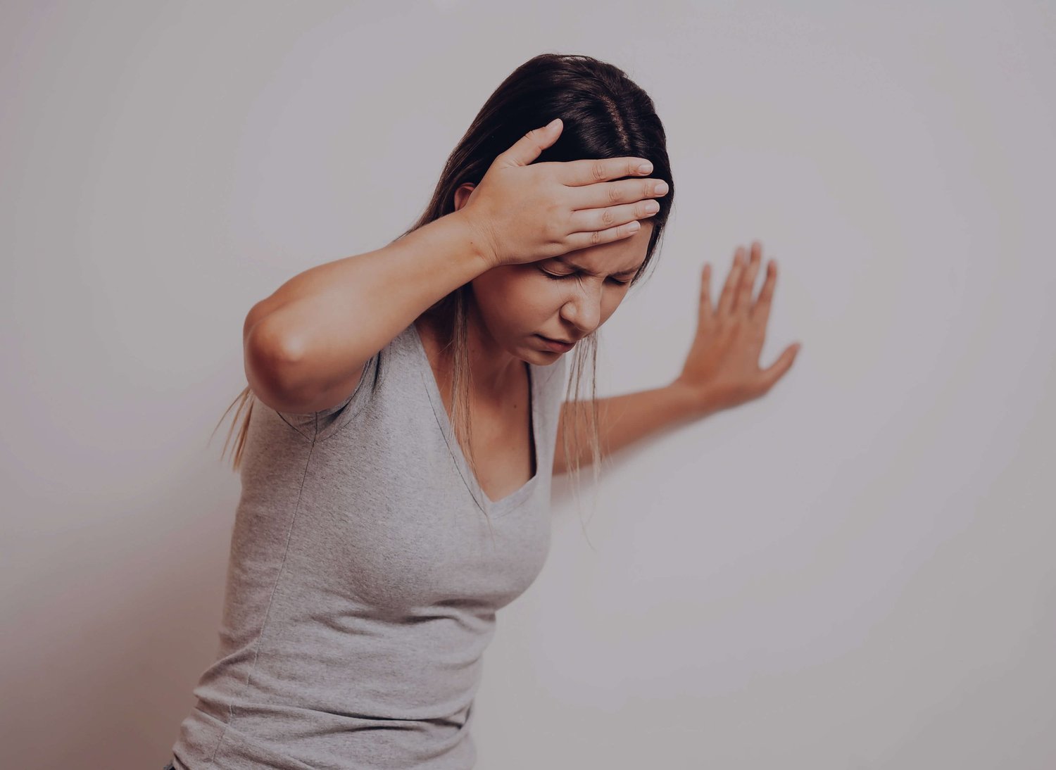Woman holding her head and steadying herself against a wall during a dizzy spell