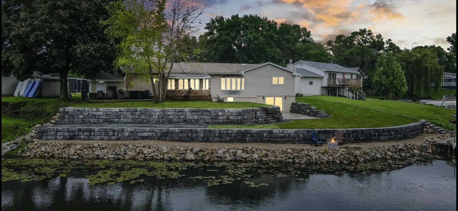 Aerial sunset view of Grand Ledge terraced walls stepping down from a home to a waterfront, with a lone chair at the water's edge