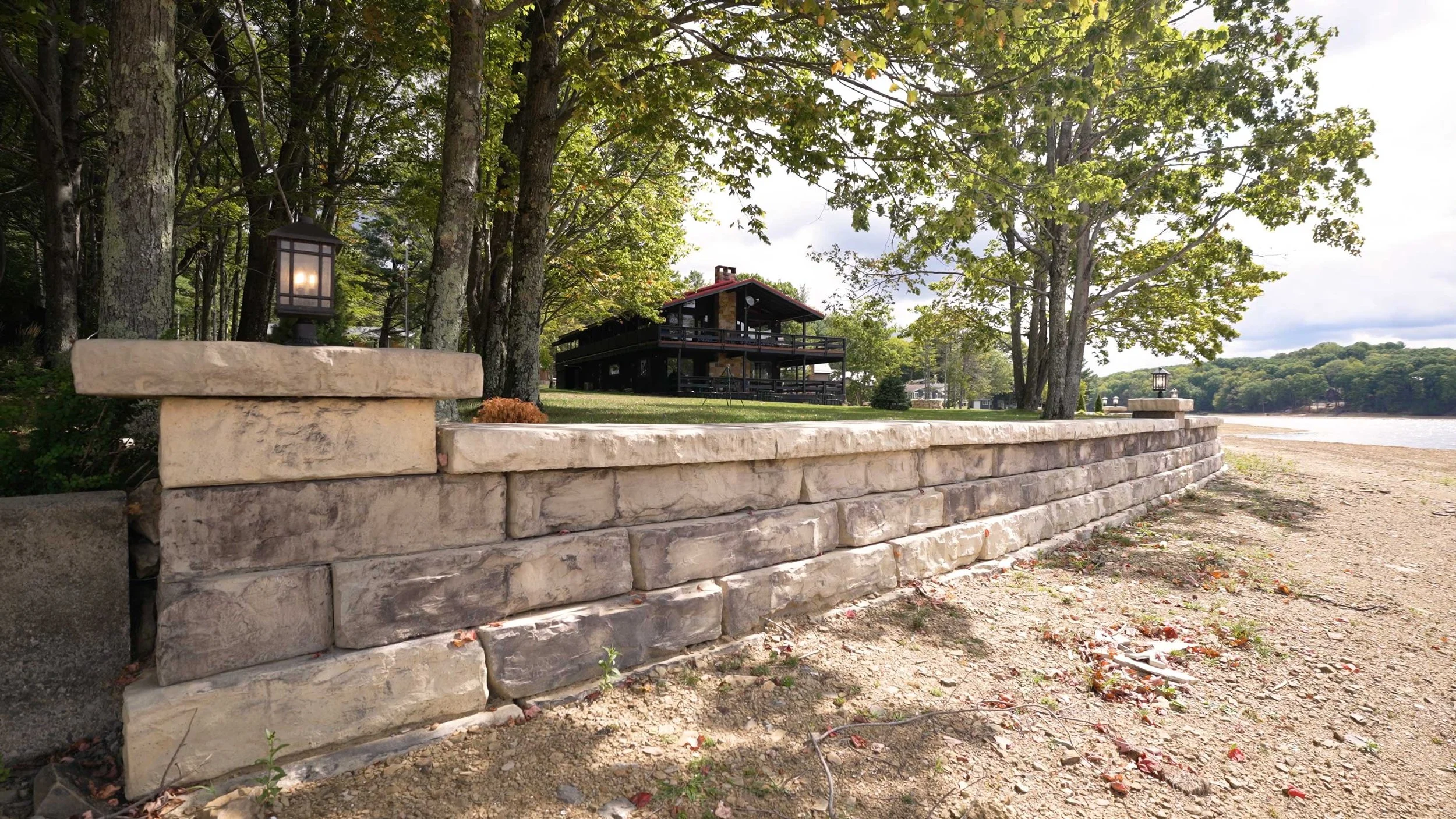Grand Ledge retaining wall running along a lakefront shoreline, with a cabin-style home visible through the trees