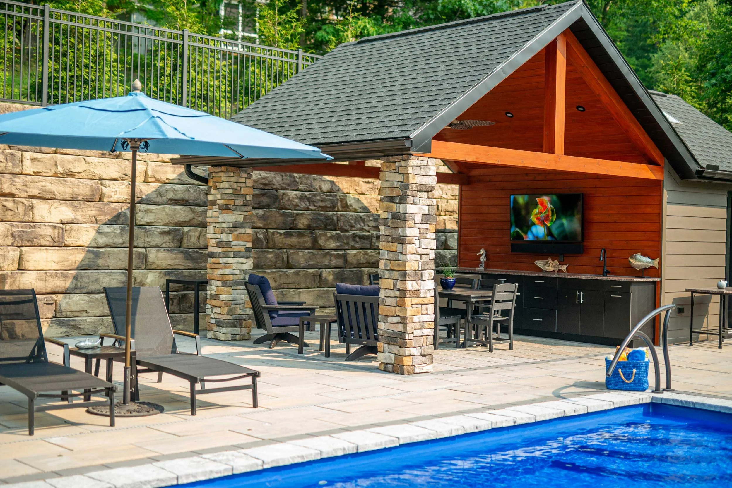 Luxury pool area backed by a Grand Ledge retaining wall, with outdoor pavilion, kitchen, and dining area