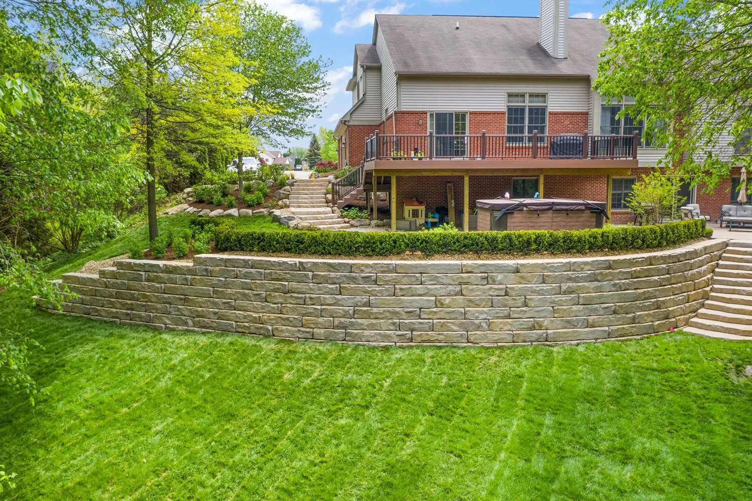 Curved Grand Ledge terraced retaining walls wrapping the back of a residential home, with lush lawn and garden beds