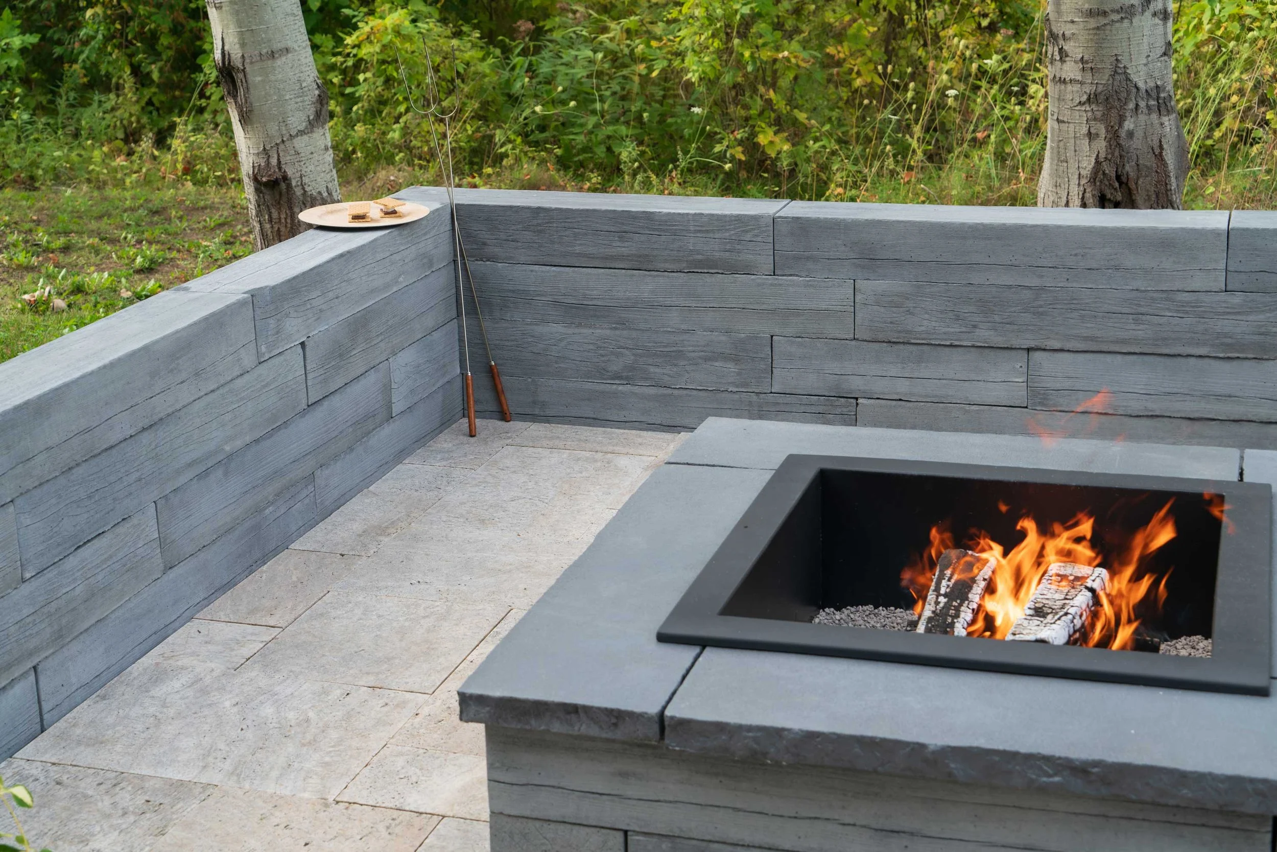 Heartwood freestanding wall encircling a backyard fire pit, set for s'mores and outdoor entertaining
